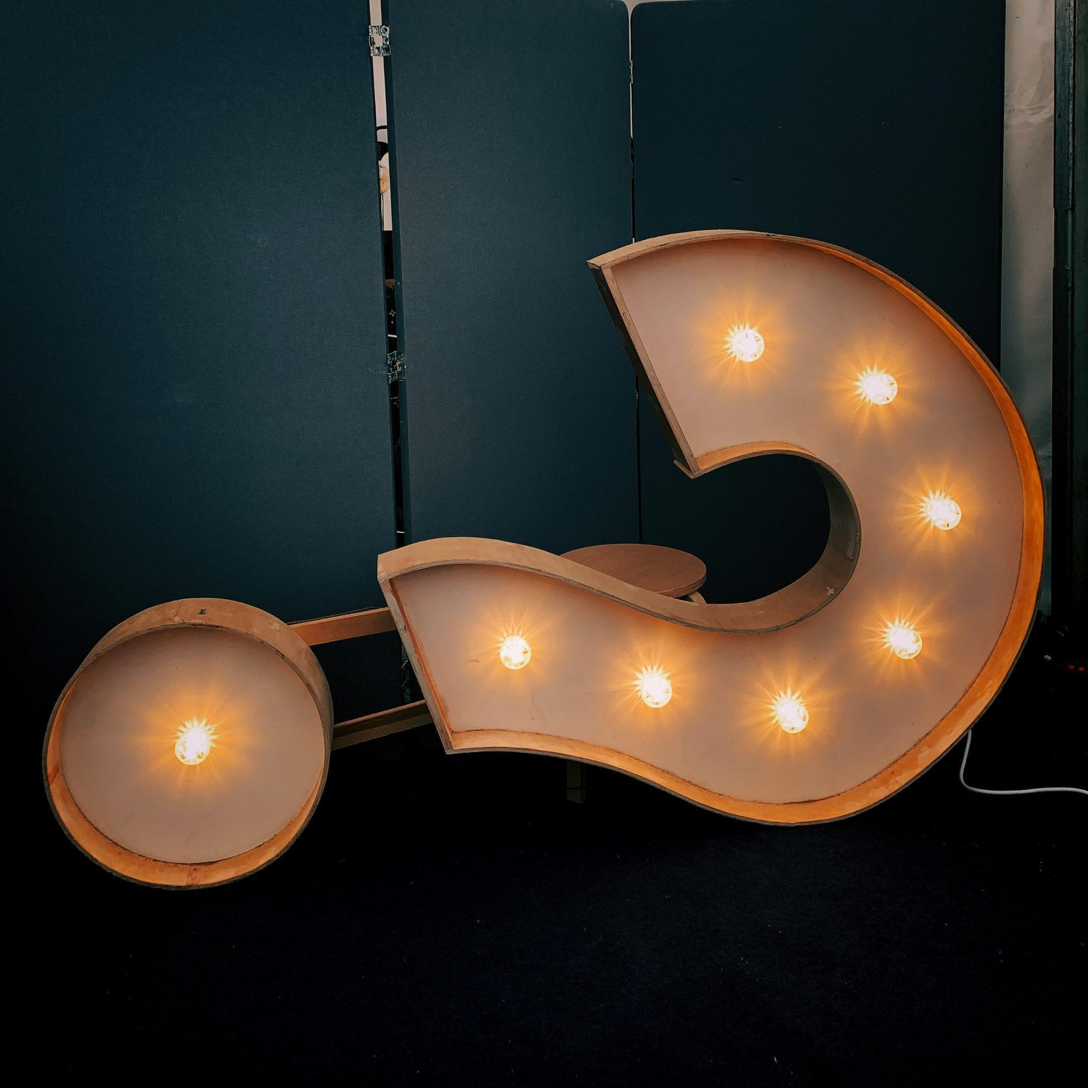 Giant question mark sign with lights, laying on its side with a dark background